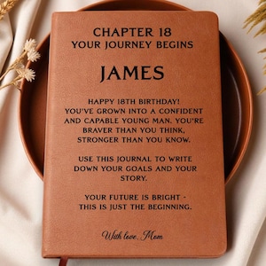 May include: A tan leather-like journal with black engraved text that reads: CHAPTER 18 YOUR JOURNEY BEGINS, JAMES, HAPPY 18TH BIRTHDAY! YOU'VE GROWN INTO A CONFIDENT AND CAPABLE YOUNG MAN. YOU'RE BRAVER THAN YOU THINK, STRONGER THAN YOU KNOW. WITH LOVE, MOM.