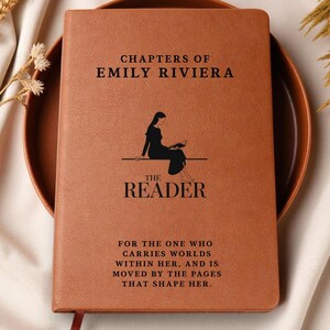 May include: A brown journal with the text "CHAPTERS OF EMILY RIVIERA" and "THE READER" printed on the cover. A silhouette of a person reading is in the center. The journal also has the quote: "FOR THE ONE WHO CARRIES WORLDS WITHIN HER, AND IS MOVED BY THE PAGES THAT SHAPE HER."