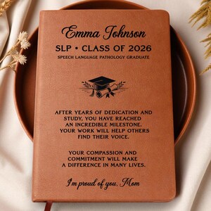 May include: A brown leather-bound journal with the name "Emma Johnson" and "SLP CLASS OF 2026" printed on the cover. The journal includes text about dedication and helping others. A graduation cap and scroll graphic is also present.