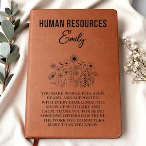 May include: A brown leather-bound journal with the words "HUMAN RESOURCES" and the name "Emily" embossed on the cover. Below the name is a floral design. The journal has a quote about appreciation for HR professionals.