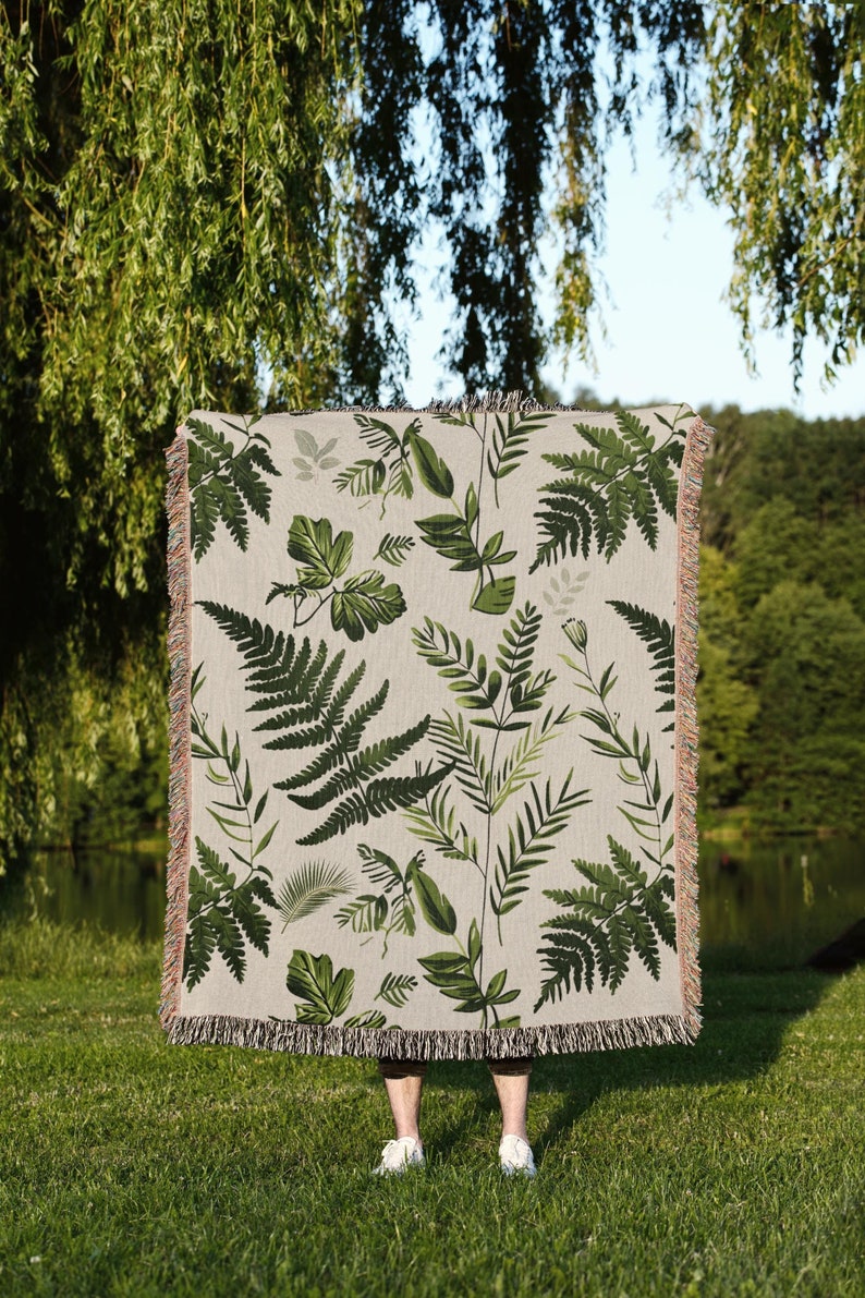 Botanical plant woven blanket with green fern and leaf print on cream, fringed edge.