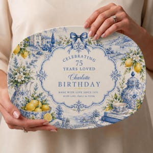 May include: An oval ceramic platter featuring a blue and white toile pattern with yellow lemons. The center text reads CELEBRATING 75 YEARS LOVED, Charlotte BIRTHDAY, MADE WITH LOVE SINCE 1951, WITH LOVE, EMILY & PETER. It includes illustrations of a pitcher, bowl, and tea set.