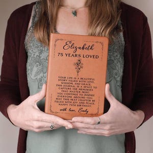 May include: A tan-coloured journal with the inscription "Elizabeth 75 YEARS LOVED" and a floral design. The journal's cover features a personal message. A thoughtful gift for a 75th birthday.