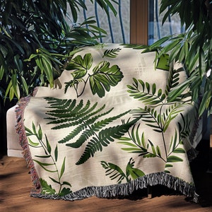 Botanical plant woven blanket with green fern and leaf print on cream, fringed edge.