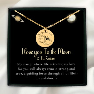 以下が含まれることがあります： 「Love You to the Moon & To Saturn」という文字が書かれた月と惑星の丸いペンダントが付いたゴールドネックレス。ネックレスは白地に黒の箱に入っていて、「I love you To the Moon & To Saturn. No matter where life takes us, my love for you will always remain strong and true, a guiding force through all of life's ups and downs.」という文字が書かれている。