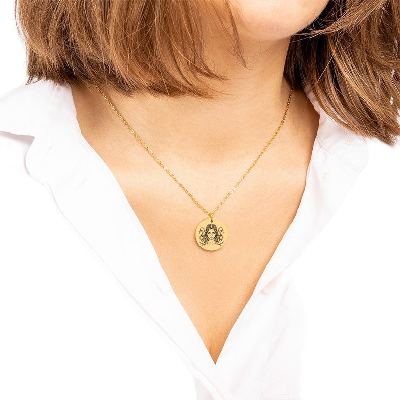 May include: A gold chain necklace with a round pendant featuring a black and white illustration of a woman with long hair.