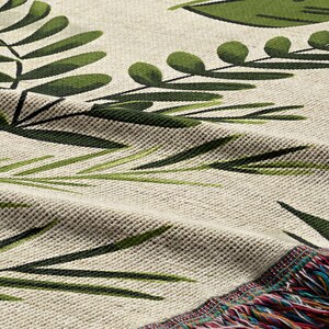 Botanical plant woven blanket with green fern and leaf print on cream, fringed edge.