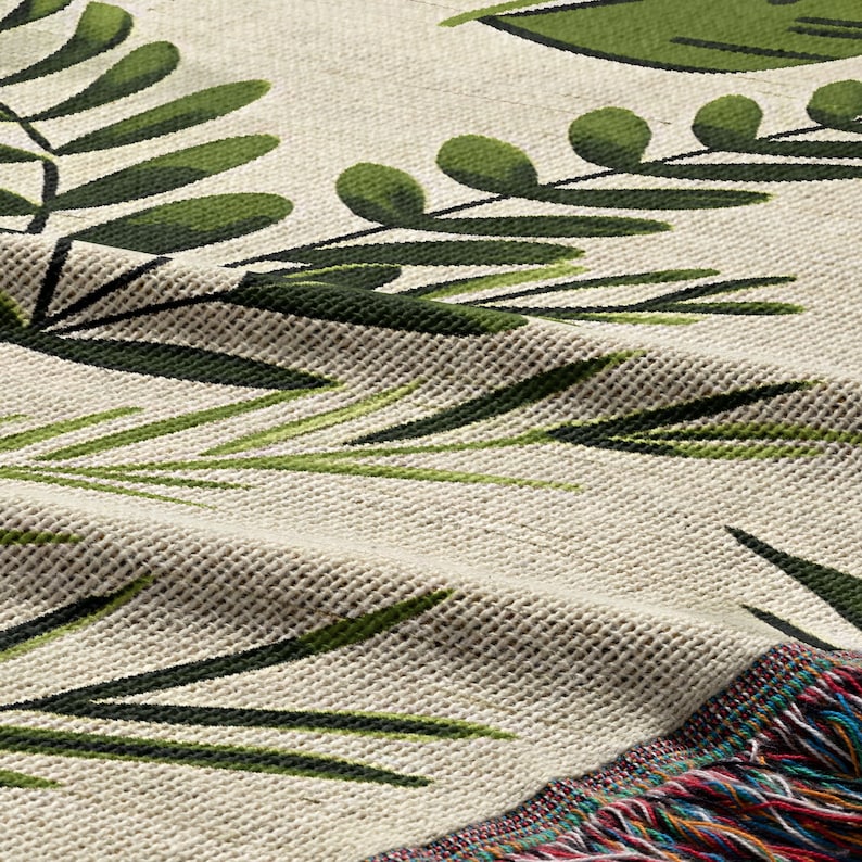 Botanical plant woven blanket with green fern and leaf print on cream, fringed edge.
