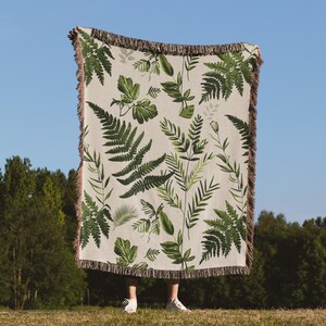 Botanical plant woven blanket with green fern and leaf print on cream, fringed edge.