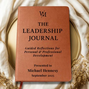 May include: A brown leather journal with the text "THE LEADERSHIP JOURNAL" and "Guided Reflections for Personal & Professional Development" printed on the front cover. The journal is presented to Michael Hennesy in September 2025.
