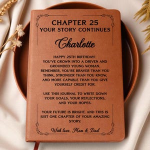 May include: A tan leather-bound journal featuring black engraved text that reads: CHAPTER 25 YOUR STORY CONTINUES, Charlotte, HAPPY 25TH BIRTHDAY! YOU'VE GROWN INTO A DRIVEN AND GROUNDED YOUNG WOMAN. REMEMBER, YOU'RE BRAVER THAN YOU THINK, STRONGER THAN YOU KNOW, AND MORE CAPABLE THAN YOU GIVE YOURSELF CREDIT FOR. USE THIS JOURNAL TO WRITE DOWN YOUR GOALS, YOUR REFLECTIONS, AND YOUR HOPES. YOUR FUTURE IS BRIGHT, AND THIS IS JUST ONE CHAPTER OF YOUR AMAZING STORY. With love, Mom & Dad.