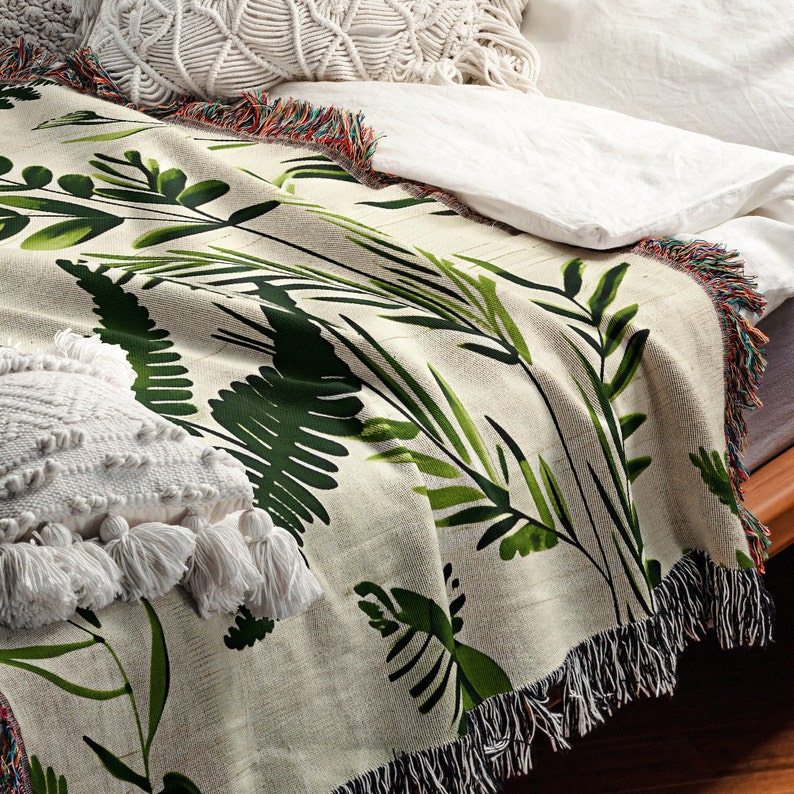 Botanical plant woven blanket with green fern and leaf print on cream, fringed edge.