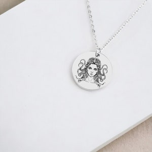 May include: A silver necklace with a round pendant featuring a black and white illustration of Medusa, a Greek mythological figure with snakes for hair.