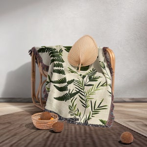 Botanical plant woven blanket with green fern and leaf print on cream, fringed edge.