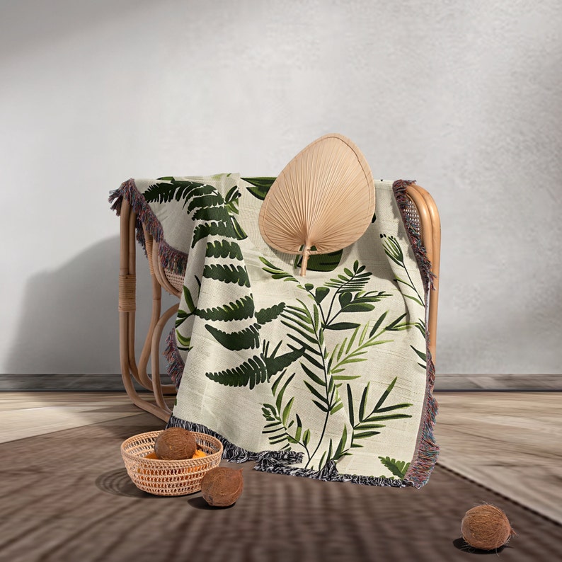Botanical plant woven blanket with green fern and leaf print on cream, fringed edge.
