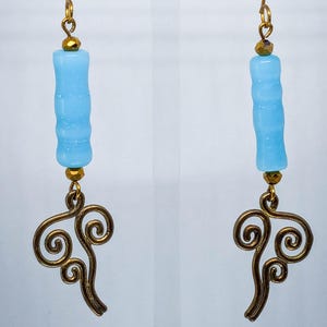 May include: A pair of earrings with light blue cylindrical beads and bronze-coloured, swirling charms. The earrings have gold-coloured ear wires and small gold beads. The charms have an ornate design.