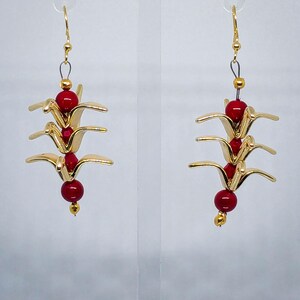 May include: Gold-colored dangle earrings featuring a layered origami crane design. Each earring has three gold cranes, accented with red beads. The earrings hang from gold-colored hooks.
