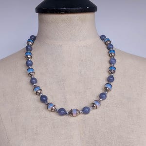 May include: A necklace made of blue and silver beads. The beads are round and have a slight iridescent sheen. The necklace is on a white mannequin.