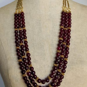 May include: A multi-strand necklace with four rows of dark red gemstone beads and gold accents.
