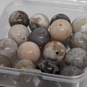 Può includere: Un contenitore di perline di agata assortite in tonalità di grigio, bianco e rosa. Le perline sono rotonde e hanno una finitura liscia e lucida.