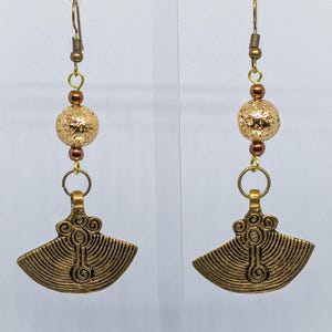 以下が含まれることがあります： ゴールドカラーのぶら下がりイヤリングのペア。各イヤリングは、テクスチャードゴールドビーズ、小さな茶色のビーズ、詳細なデザインの扇形のペンダントが特徴です。イヤリングはゴールドカラーのイヤーフックから吊り下げられています。