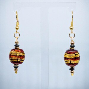 May include: Gold dangle earrings with a red and gold glass bead. The bead has a cracked gold finish and a striped pattern.