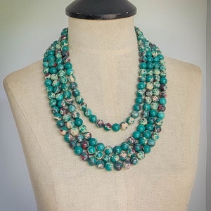 May include: A multi-strand necklace made of green and white speckled beads. The necklace is layered and has a casual, bohemian style.