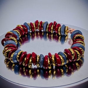 May include: A red and gray beaded bracelet with gold accents. The beads are arranged in a spiral pattern.