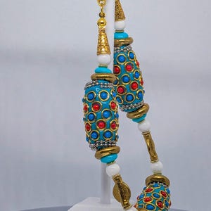 May include: A turquoise and gold beaded necklace with red and blue accents. The necklace features large, ornate beads with a geometric pattern.
