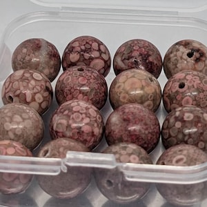 Pode incluir: Um recipiente com 18 contas redondas, salpicadas de rosa e marrom. As contas têm um diâmetro aproximado de 2,5 cm.