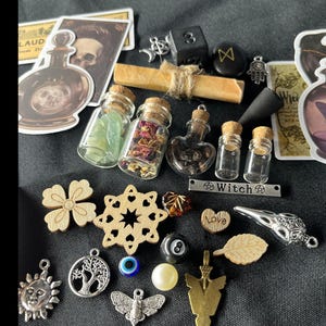 May include: A collection of mystical items, including small glass bottles with cork stoppers, wooden charms, dice, and decorative stickers. The bottles contain herbs and crystals. Other charms include a sun, tree of life, and a moth.