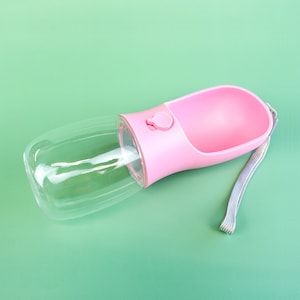 Pu&ograve; includere: Bottiglia d'acqua in plastica rosa con un serbatoio trasparente e un cinturino grigio. La bottiglia ha un pulsante per erogare l'acqua.