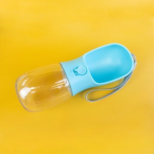 Pu&ograve; includere: Una bottiglia d'acqua in plastica blu e trasparente con una ciotola integrata per cani. La bottiglia ha una tracolla per il trasporto.