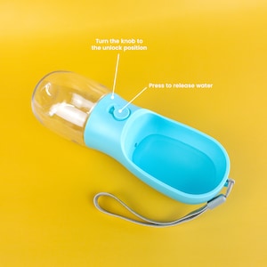 Pu&ograve; includere: Una bottiglia d'acqua per cani in plastica blu e trasparente con un cinturino. La bottiglia ha un pulsante per rilasciare l'acqua e una manopola per sbloccare il flusso d'acqua.