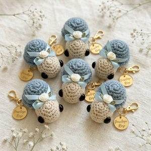 May include: Six crocheted snail keychains featuring blue shells and beige bodies. Each snail has a light blue ribbon bow with a small white flower, black bead eyes, a gold-tone lobster clasp, and a round gold charm engraved with Penelope Rose.