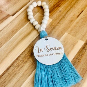 May include: A white wooden bead garland with a blue tassel and a round white wooden sign that says "In Session Please do not Disturb".