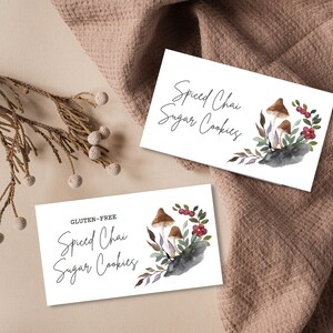 May include: Two white cards with the text "Spiced Chai Sugar Cookies" and "Gluten-Free Spiced Chai Sugar Cookies" in black script. The cards feature a watercolor illustration of mushrooms, berries, and leaves.