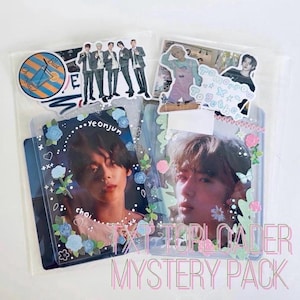 May include: A TXT mystery pack containing two clear plastic top-loaders holding photo cards of Yeonjun and Beomgyu. The cards are decorated with blue and pink floral stickers, stars, and hearts. Includes additional stickers of the group members.