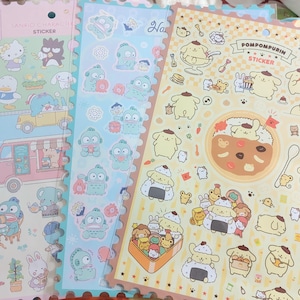 Op de afbeelding: Vellen Sanrio-personagestickers. De stickers bevatten personages als Hello Kitty en Pompompurin. De stickers zijn in pastelkleuren, met een verscheidenheid aan vormen en maten. De stickers zitten op geperforeerde vellen.
