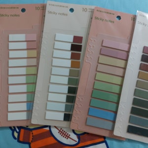 Puede incluir: Un conjunto de diez paquetes de notas adhesivas con diferentes combinaciones de colores. Cada paquete tiene diez notas con un borde blanco y una franja de color. Los colores incluyen rosa, beige, verde, azul, marrón y gris.