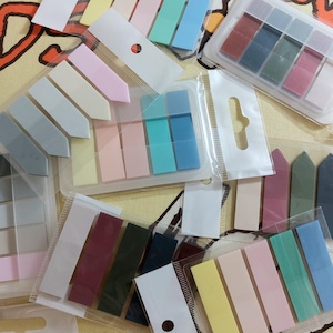 Könnte beinhalten: Sortiment an bunten Haftnotizen in verschiedenen Formen und Größen. Die Notizen sind in durchsichtigen Plastiktüten verpackt. Die Notizen eignen sich perfekt zum Markieren von Seiten, Hervorheben wichtiger Informationen und zum Hinzufügen eines Farbakzents zu Ihren Notizen.