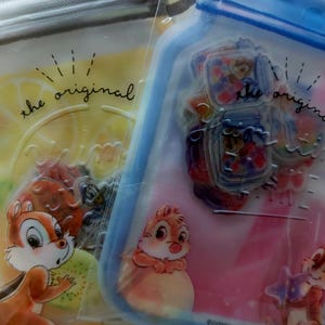 May include: Two clear plastic zip-top bags with colorful illustrations. One bag is yellow with a lemon design and a cartoon chipmunk. The other is blue with a jar design and two chipmunks. Text reads "the original time".