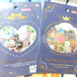 Op de afbeelding: Twee blauwe en gouden sticker vellen met een hartvormig ontwerp. Elk vel heeft een verscheidenheid aan kleurrijke cartoonfiguren en de tekst "Sanrio Characters" en "Ik denk dat je de beste vriend ter wereld bent!"