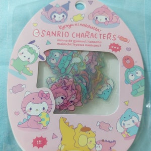 Op de afbeelding: Een roze en witte vel met stickers waarop Sanrio-karakters zijn gekleed als dinosaurussen. De stickers zijn transparant en hebben een holografisch effect. Het vel is verpakt in een doorzichtige plastic zak. De tekst op het vel luidt "Sanrio Characters Kyoryu ni natchatta! Minna de gyaooo!! Tanoshii mainichi! Kyowa nanisuru?"