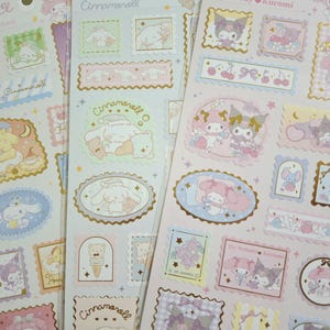May include: Sheets of stickers featuring various Sanrio characters in pastel colors. Designs include Cinnamoroll, My Melody, and Kuromi, with decorative frames and illustrations. The stickers have a variety of shapes and sizes, with gold foil accents.
