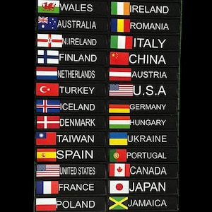 Könnte beinhalten: Ein Set aus 20 bunten Stoff-Patches mit Flaggen verschiedener Länder, darunter Großbritannien, Schweden, Schottland, Russland, Wales, Irland, Australien, Rumänien, Nordirland, Italien, Finnland, China, Niederlande, Österreich, Türkei, USA, Island, Deutschland, Dänemark, Ungarn, Taiwan, Ukraine, Spanien, Portugal, Vereinigte Staaten, Kanada, Frankreich, Japan, Polen, Jamaika, Belgien und England. Die Patches sind in zwei Spalten auf einem schwarzen Hintergrund angeordnet. Ein Satz silberner Schlüsselringe befindet sich am unteren Rand des Bildes.