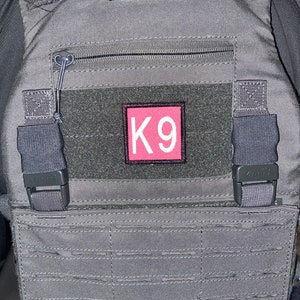 May include: A gray tactical vest with a zippered pocket and a pink patch that says "K9".