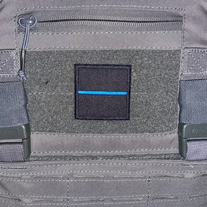 Puede incluir: Una mochila táctica gris con un parche negro que presenta una línea azul delgada. La mochila tiene dos correas ajustables con hebillas negras que dicen "Viper".