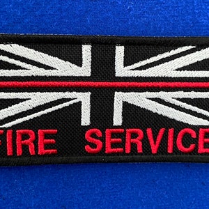 Könnte beinhalten: Ein schwarzer Patch mit einem weißen Union-Jack-Design und einem roten Streifen in der Mitte. Die Worte "FIRE SERVICE" sind in Rot unter der Flagge gestickt.