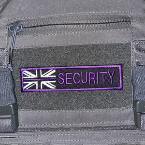 May include: A grey tactical vest with a black zipped pocket and a purple patch that says "SECURITY" with a white Union Jack flag design.